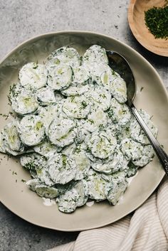 a white plate topped with cucumber salad next to a bowl of parsley