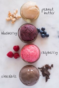 three different types of ice cream in bowls on a table with berries, nuts and chocolate