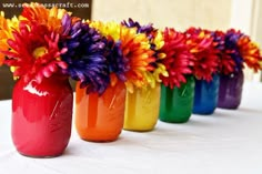 colorful vases with flowers in them lined up on a table