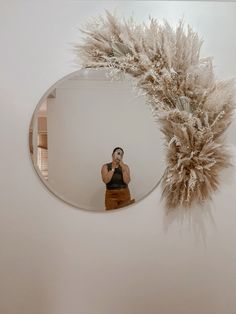 a woman taking a selfie in front of a mirror with feathers on the wall