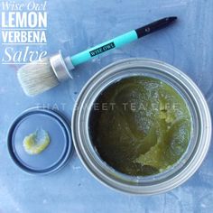 a jar filled with green liquid next to a paintbrush and container full of lemon verbena salve