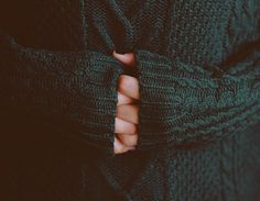 a person with their hand on the pocket of a green sweater that is rolled up