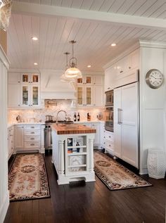 a large kitchen with white cabinets and wooden flooring, along with a clock on the wall