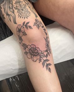 a woman's leg with tattoos on it and flowers around her ankles, sitting on a bed