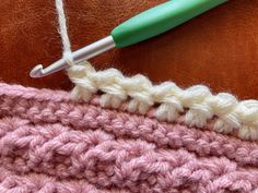 the crochet stitch is being worked on with a green handled crochet hook