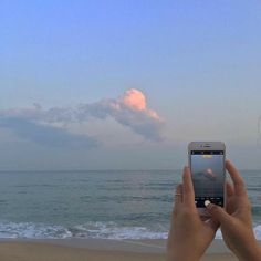 someone taking a photo on their cell phone at the beach with clouds in the sky