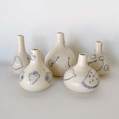 four white vases with blue designs on them are lined up against a white wall