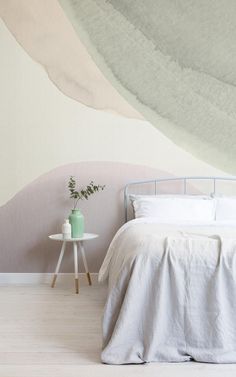 a white bed sitting next to a table with a green vase on top of it