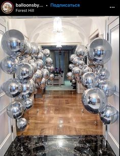 a bunch of shiny silver balloons hanging from the ceiling in an entry way with wood flooring