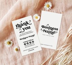 two business cards sitting on top of a bed next to some daisies and flowers