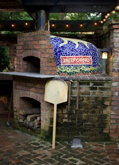 an outdoor brick pizza oven with blue mosaic tiles and lights hanging from it's roof