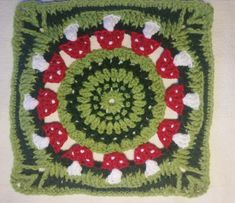 a crocheted square with red and white mushrooms in the center on a table