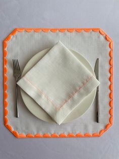 a white plate with an orange border on it and silverware next to the napkin