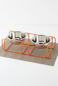 two metal bowls sitting on top of an orange stand