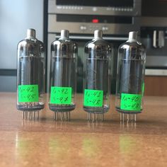 four tubes with green labels on them sitting on a table in front of a microwave