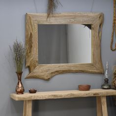 a wooden table topped with a mirror next to a vase filled with dried flowers and plants