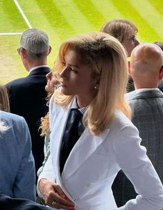 a woman in a white suit and tie at a tennis match