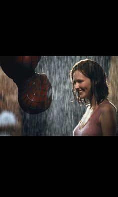 a woman standing in the rain next to a spider - man mask on her head