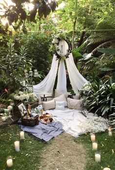 an outdoor area with candles and flowers on the ground, surrounded by greenery that is covered in white sheer curtains