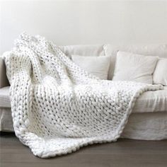 a white couch with a knitted blanket on it's back next to pillows