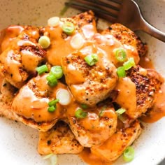 a white plate topped with chicken covered in gravy and green onions next to a fork