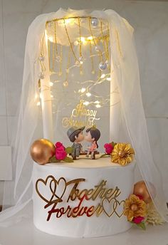 a wedding cake decorated with gold and white frosting, surrounded by flowers and lights