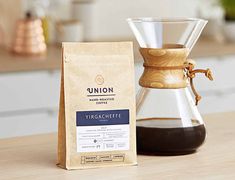 a bag of coffee next to a glass carafe on a counter