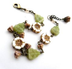 Gorgeous woodsy flower and leaf bead bracelet - Czech glass beads wire-wrapped together in antiqued brass look like an earthy garland for your wrist. Cream, brown and green colors. Featuring rustic-looking creamy white and brown accented Picasso flat flowers (12mm), with streaky yellow-green leaves and tiny 4x6mm gold-lustered topaz pink bell flowers Composition: -There are 3 large cream flat flowers - one at the centre with a leaf each side.  -From the leaf each side of the central flower, dangle 2 baby bell flowers.  -Another one each side linked sideways, and then another flat flower with another leaf. -Flowers and leaves are finished with 4mm lustered champagne Czech fire-polished glass crystal at each end. Closes with a lobster clasp, and has a 1" extension chain with a flower bead da Czech Beads Jewelry, Cream Flats, Woodland Jewelry, Feminine Jewelry, Leaf Bracelet, Bead Garland, Flower Leaf, Rust Orange, Beaded Garland