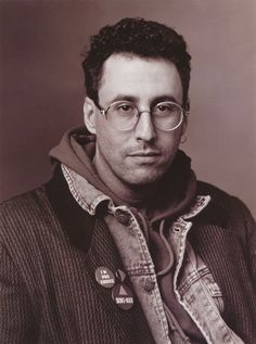 a black and white photo of a man with glasses wearing a jacket, sweater and scarf