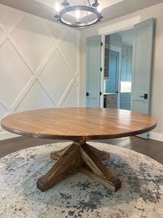 a round wooden table sitting on top of a rug in a room with white walls