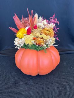 an orange pumpkin vase filled with flowers on top of a black surface in front of a blue background