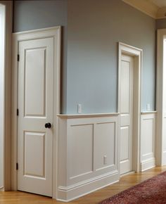 an empty room with white paneling and wood flooring on the walls, along with a red rug