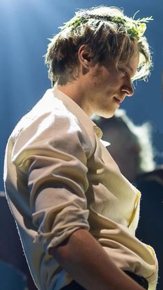 a young man with a flower crown on his head is standing in front of a microphone