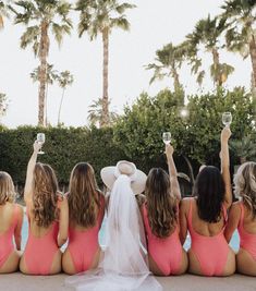 the bridesmaids are sitting by the pool and holding their hats in the air