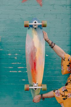 a woman holding up a skateboard in front of a blue wall