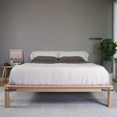 a bed with white linens and pillows in a gray room next to a potted plant