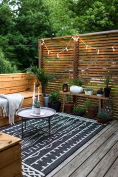 an outdoor deck with potted plants and lights strung on the fence behind it,