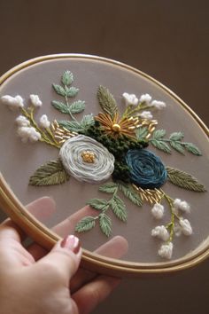 someone is holding up a small embroidery project with flowers and leaves on the front of it