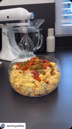 a glass bowl filled with food sitting on top of a counter next to a blender