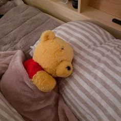 a winnie the pooh stuffed animal laying on top of a bed under a blanket