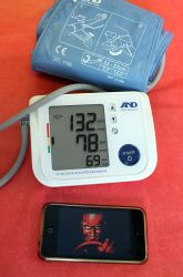 an electronic blood pressure meter next to a cell phone on a red bed with a blue bag