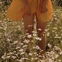 a woman in an orange dress is standing in a field with daisies and flowers