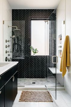 a bathroom with black and white tile, glass shower door, and rug on the floor