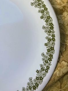 a white plate with green designs on the rim and bottom, sitting on a gold cloth