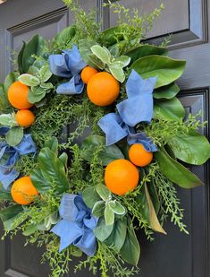 a wreath with oranges and green leaves hanging on a front door, decorated with blue ribbon