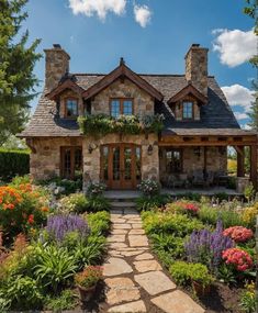 a stone house with lots of flowers and plants around it's front entrance, surrounded by greenery