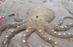 an octopus made out of sand on the beach with beads and shells attached to it