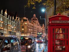 a red phone booth sitting on the side of a street next to tall buildings at night