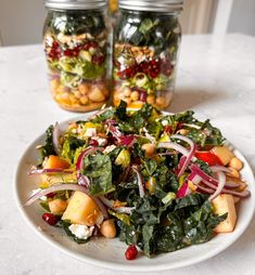 a white plate topped with salad next to two mason jars filled with vegetables and nuts