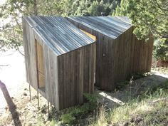 two wooden buildings sitting on top of a grass covered hillside next to trees and bushes